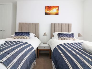 A bedroom with two single beds blue striped blankets and a nightstand with a lamp in Saltwater One Lusty Glaze Newquay