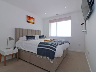 A bedroom with a beige bed a striped blanket a side table with a lamp and a window at Saltwater One Lusty Glaze in Newquay