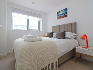 A bedroom with a bed with pillows and folded towels a bedside table with a lamp and a window at Saltwater One Lusty Glaze in Newquay
