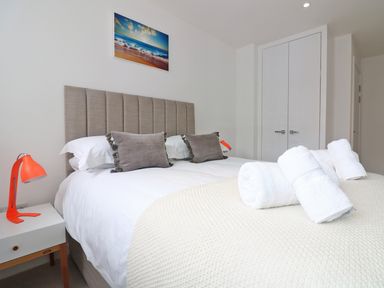 A bedroom with a bed with pillows and rolled towels bedside tables with lamps and a painting above the bed at Saltwater One Lusty Glaze in Newquay