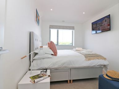 A bedroom with a bed pillows bedside table lamp window and wall mounted TV at Saltwater One Lusty Glaze Newquay