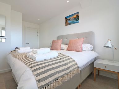 A bedroom with a bed with pillows and folded towels a bedside table with a lamp and a picture on the wall at Saltwater One Lusty Glaze in Newquay