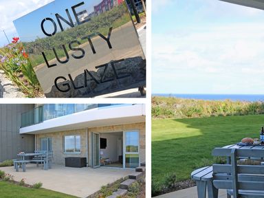 A sign with one lusty glaze text a patio with outdoor table and chairs and a view of grass and sea at Saltwater One Lusty Glaze in Newquay