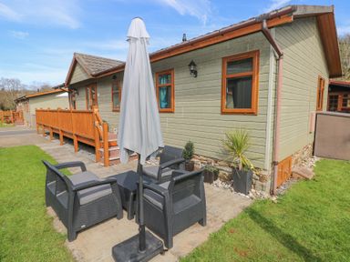 An outdoor seating area with black chairs a table and a closed umbrella next to a green house with wooden windows at Heddwch Wisemans Bridge near Saundersfoot