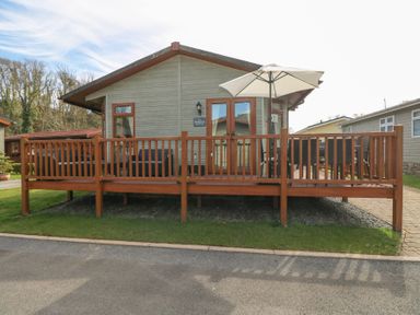 A single story cabin with a wooden deck and patio umbrella at Heddwch Wisemans Bridge near Saundersfoot
