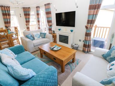 A living room with blue and beige sofas a wooden coffee table and a wall-mounted television at Heddwch Wisemans Bridge near Saundersfoot