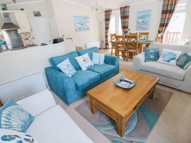 A living room with blue and white sofas and a wooden coffee table next to a dining area with wooden chairs at Heddwch Wisemans Bridge near Saundersfoot