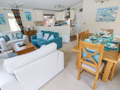A living room with sofas and pillows next to a dining table set with plates and glasses at Heddwch Wisemans Bridge near Saundersfoot