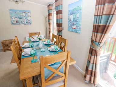 A dining room with a wooden dining table set for six with green glasses and blue placemats and striped curtains at Heddwch Wisemans Bridge near Saundersfoot