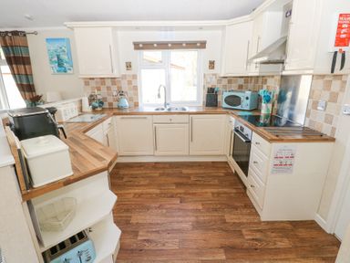 A kitchen with wooden countertops and cream cabinets with a window above the sink at Heddwch Wisemans Bridge near Saundersfoot