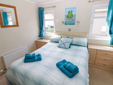 A bedroom with a double bed blue towels on the bed a painting above the bed blue curtains and wooden bedside tables at Heddwch Wisemans Bridge near Saundersfoot