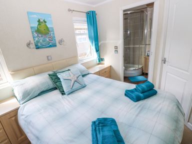 A bedroom with a bed blue pillows teal towels and a door leading to a bathroom at Heddwch Wisemans Bridge near Saundersfoot