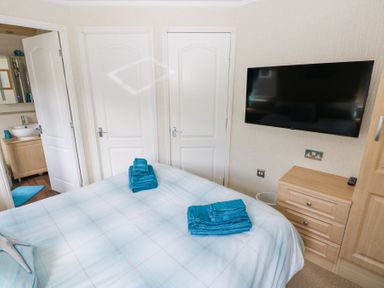 A bedroom with a bed with folded teal towels and a wall-mounted TV at Heddwch Wisemans Bridge near Saundersfoot