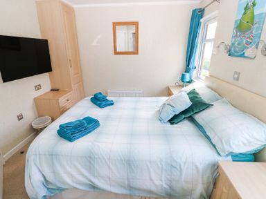 A bedroom with a bed with folded blue towels pillows and a mounted television at Heddwch Wisemans Bridge near Saundersfoot