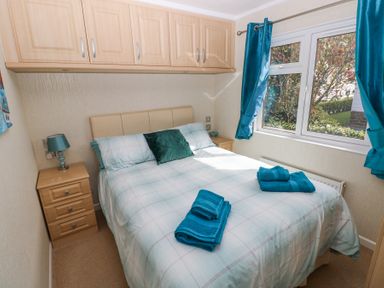 A bedroom with a bed bedside tables overhead cabinets and teal towels on the bed at Heddwch Wisemans Bridge near Saundersfoot