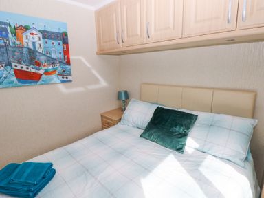 A bedroom with a double bed a green cushion folded towels a bedside table with lamp and a painting on the wall at Heddwch Wisemans Bridge near Saundersfoot