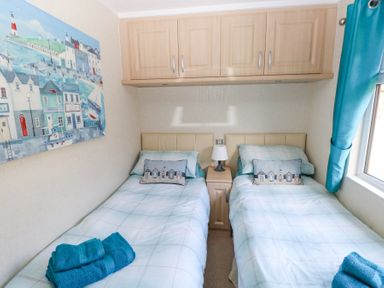 A bedroom with two single beds a bedside table with lamp and overhead cabinets at Heddwch Wisemans Bridge near Saundersfoot