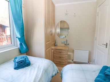A bedroom with two single beds blue towels on beds a wooden wardrobe a chest of drawers and a window at Heddwch Wisemans Bridge near Saundersfoot