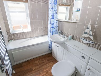 A bathroom with a bathtub shower curtain sink toilet cabinet and a model sailboat on the countertop at Heddwch in Wisemans Bridge near Saundersfoot