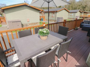 An outdoor patio with a dining table and chairs a potted plant on the table umbrella and cottages in the background at Heddwch Wisemans Bridge near Saundersfoot