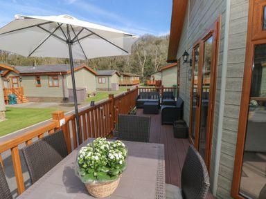 An outdoor deck with a table and chairs under an umbrella and seating area on a wooden deck at Heddwch Wisemans Bridge near Saundersfoot
