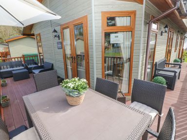 An outdoor deck with a dining table and chairs and seating area with armchairs and a bench at Heddwch Wisemans Bridge near Saundersfoot