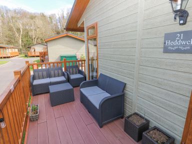 An outdoor wooden deck with dark wicker seating and planters at Heddwch Wisemans Bridge near Saundersfoot