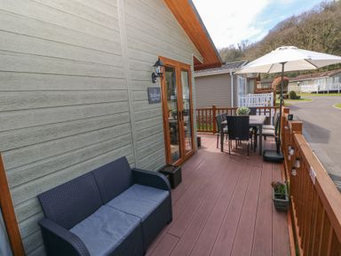 A wooden deck with a sofa table chairs an umbrella and potted plants outside a building at Heddwch Wisemans Bridge near Saundersfoot