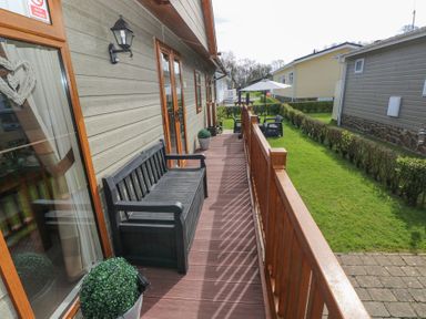 An outdoor wooden deck with a black bench and potted plants next to a house with wooden siding and windows at Heddwch Wisemans Bridge near Saundersfoot