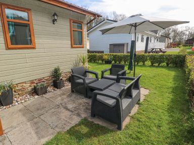 A patio area with black wicker chairs and a table under a large umbrella next to a beige house at Heddwch Wisemans Bridge near Saundersfoot