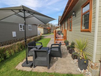An outdoor patio area with black wicker chairs and a table under a large grey umbrella next to a beige building with wooden windows at Heddwch Wisemans Bridge near Saundersfoot