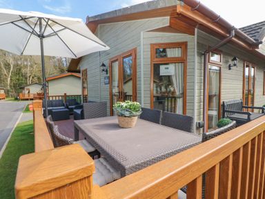 An outdoor deck with a dining table and chairs an umbrella and additional seating at Heddwch Wisemans Bridge near Saundersfoot