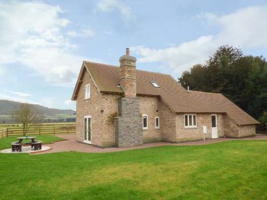 A brick house with a chimney and a picnic table in a grassy yard at Rose Cottage in Winforton near Hay-on-Wye