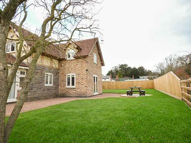 A fenced garden with a picnic table and a tree beside a brick house at Rose Cottage in Winforton near Hay-on-Wye