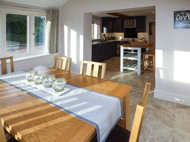 A dining area with wooden table and chairs and an open kitchen with dark cabinets at Rose Cottage Winforton near Hay-on-Wye
