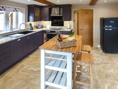 A kitchen with dark cabinets a wooden island table with stools and a black refrigerator at Rose Cottage in Winforton near Hay-on-Wye