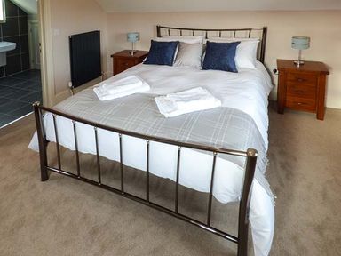 A bedroom with a metal bed frame with white and gray bedding two wooden bedside tables with lamps and towels on the bed at Rose Cottage in Winforton near Hay-on-Wye