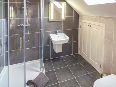 A bathroom with a corner shower enclosure a wall-mounted sink and storage cabinets under a sloped ceiling at Rose Cottage Winforton near Hay-on-Wye