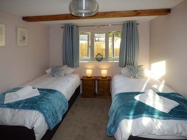 A bedroom with two single beds bedside tables with lamps and a window with blue curtains at Rose Cottage in Winforton near Hay-on-Wye