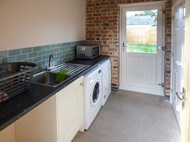 A utility room with a sink washing machine dryer microwave and a door leading outside at Rose Cottage in Winforton near Hay-on-Wye