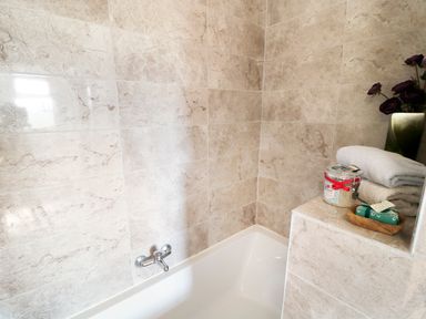 A bathroom corner with a bathtub and beige tiled walls with towels a jar and soap at View The Gallery in Okehampton
