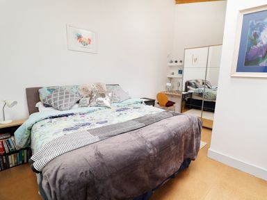 A bedroom with a bed covered in patterned bedding and pillows with a mirrored wardrobe and a small desk with a chair at View The Gallery in Okehampton