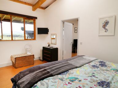 A bedroom with a bed a chest a dresser with a mirror a wall-mounted TV and a window at View The Gallery in Okehampton