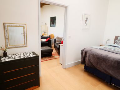 A bedroom with a bed and a chest of drawers and a view into a living room with black sofas at View The Gallery in Okehampton