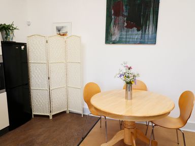 A dining area with a wooden round table and chairs flowers in a vase on the table a folding room divider a black refrigerator and artwork on the walls at View The Gallery in Okehampton
