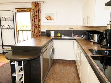 A kitchen with countertop appliances and a washing machine near a door with floral curtains at View The Gallery in Okehampton