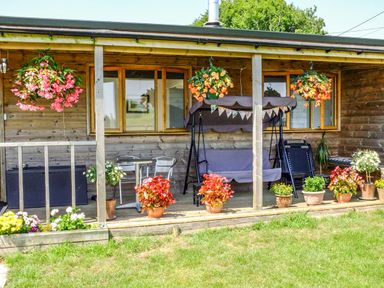 A wooden porch with hanging and potted flowers metal table with chairs and a swing seat at View The Gallery in Okehampton