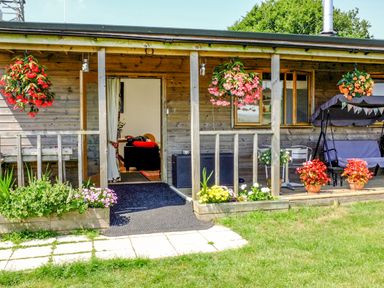 A wooden porch with hanging flower baskets potted plants a swing seat and an open door at View The Gallery in Okehampton