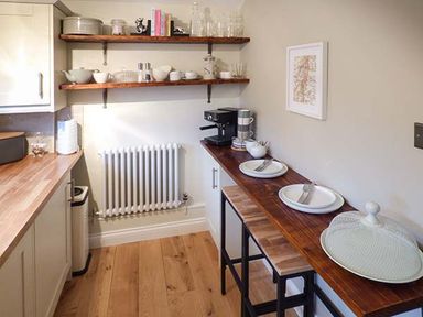 A kitchen with wooden floors wooden shelves and a wooden breakfast bar with plates cups and an espresso machine at Kitts Cottage in Little Malvern near Malvern