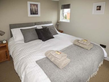 A bedroom with a made bed pillows towels bedside tables and framed pictures on the wall at Kitts Cottage in Little Malvern near Malvern